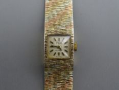 A LADY'S NINE CARAT TRI-COLOUR GOLD ENCASED AVIA WRISTWATCH having a square dial and an incorporated