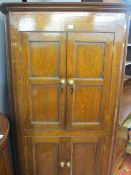 AN ANTIQUE OAK ONE PIECE STANDING CORNER CUPBOARD, twin upper and lower panel fronted doors of peg-