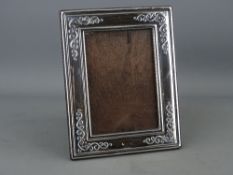 A MODERN SILVER EASEL PORTRAIT FRAME with scrolled decoration to take a picture 12 x 8.5 cms