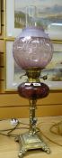 An antique cherubic brass oil lamp on four scroll feet and with dimpled purple glass reservoir and
