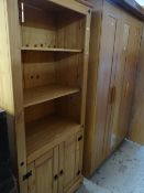 A modern pine bookshelf with cupboard base together with a modern lightwood triple wardrobe and a