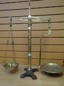An antique set of brass provision balance scales on a decorative cast iron base inscribed