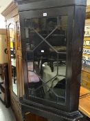 An antique single-door glazed corner cupboard on stand