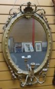 An antique gilt framed oval mirror having a shell and laurel finial and three-branch candle