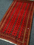 A RED GROUND RUG with geometric border and lozenge design central pattern, fringed, 200 x 117cms