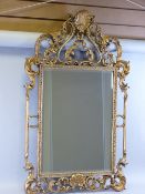 AN ORNATE FILIGREE GILT FRAMED BEVELLED EDGE WALL MIRROR with shell motifs, 108 x 66 cms overall