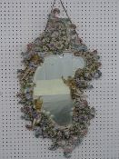 A CONTINENTAL PORCELAIN WALL MIRROR having three candle holders on a figural and floral encrusted