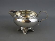 A CIRCULAR SILVER MILK/CREAM JUG with scroll handle on four fancy feet, Birmingham 1938, maker A L