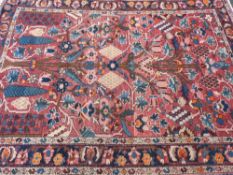 An Eastern style woollen carpet with central tree and floral design on a red ground with triple