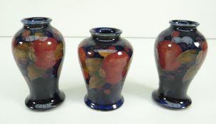 SET OF THREE MOORCROFT POTTERY SMALL VASES decorated with fruit and berries to dark blue ground