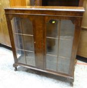 VINTAGE WALNUT TWO-DOOR DISPLAY CABINET on raised feet, with carved decoration to the top
