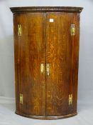 AN OAK HANGING CORNER CUPBOARD, two door, bow fronted with brass H hinges, dentil cornice and