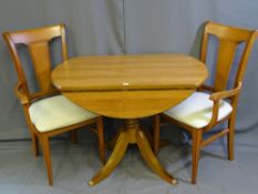 A CIRCULAR DROP LEAF LIGHTWOOD DINING TABLE with two matching upholstered arm chairs