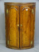 A 19TH CENTURY TWO DOOR OAK BOW FRONTED HANGING CORNER CUPBOARD, each door having applied cross