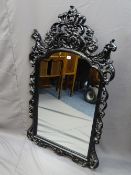 A WALL MIRROR, elaborately decorated black painted frame, 135cms height, 80cms width