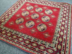 100% WOOL RED GROUND WILTON RUG with decorative nine medallion centre and geometric border, 274cms