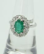 PLATINUM ILLUSION SET EMERALD AND DIAMOND CLUSTER RING, the central oval emerald (8 x 6mm)
