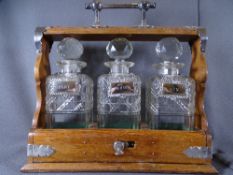 THREE BOTTLE TANTALUS with stoppers and white metal labels for port, whisky and gin