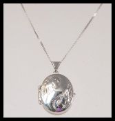 A stamped 375 white gold necklace with a spring ring clasp having a oval form locket with foliate