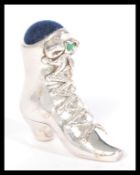 A silver pincushion in the form of a Victorian lace up boot having a blue cushion and green stone to