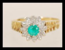 A stamped 18ct gold emerald and diamond cluster ring set with a central emerald surrounded by a
