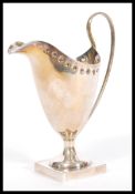 An early 20th century silver hallmarked creamer milk jug raised on square plinth base with shaped