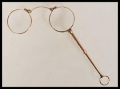A pair of early 20th Century stamped 9ct gold lignettes / handled folding glasses with round lenses.