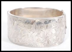 A silver hallmarked bangle bracelet having foliate engraving, with a hinged opening and safety