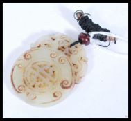 A Chinese jade roundel medallion with oriental scrolled detailing and string pendant to the top.