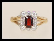 A hallmarked 9ct gold ring set with a rectangular faceted red stone with a halo of white stones.