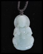 A Chinese carved jade pendant necklace in the form of a Buddha sitting in the lotus position on a