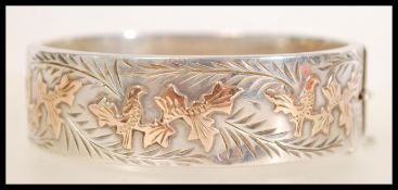 A large silver hallmarked bangle bracelet having engraved  and gold leaf design with safety chain.
