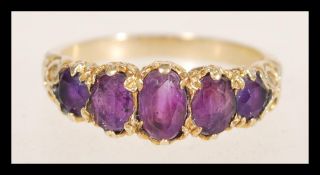 A hallmarked 9ct gold ring set with five oval purple stones with decorative scrolled shoulders.