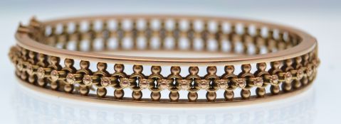 A late Victorian gold hinged bangle of openwork design decorated with beads
