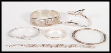 A selection of stamped silver bracelets to include a silver bangle with a hinge clasp, a dolphin