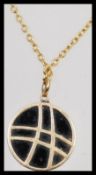 A stamped 18k gold pendant of round form set with a black stone with a cross over design, on a