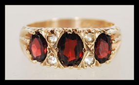 A hallmarked 9ct gold three stone garnet ting having faceted red stones with white stone spacers.