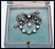 A 19th Century Victorian diamond and pearl bow brooch prong set with a central diamond to the bow of
