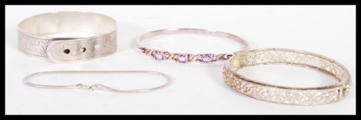 A selection of three bangles one being in the form of a belt buckle engraved with foliate, another