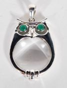 A sterling silver magnifying glass necklace pendant in the form of an owl with green stone eyes.