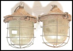 A pair of retro 20th Century industrial factory bulk cage lights, having a cast iron body, glass