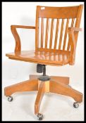 An early 20th century oak industrial office swivel captains chair raised on splayed legs with shaped
