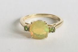 A hallmarked 9ct gold ring prong set with a round Ethiopian opal stone flanked by two green accent