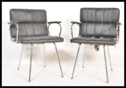 A pair of mid century retro chrome and faux black leather armchairs. Raised on chrome tubular frames