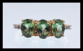 A hallmarked 9ct gold ring prong set with three oval cut green stones with white accent stones to