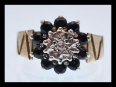 A hallmarked 9ct gold ring with a flower head set with white and blue stones and geometric engraving