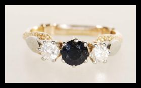A stamped 18ct gold ring prong set with a round cut sapphire flanked by two brilliant cut