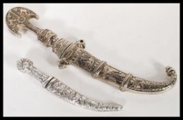 Two vintage 20th Century silver white metal daggers in sheaves comprising of a Jambiya dagger with