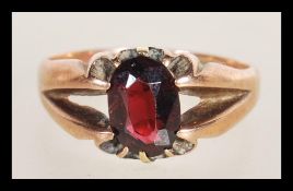 A hallmarked 9ct gold ring having a split shank design set with an oval cut garnet. Hallmarked