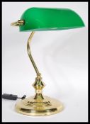 A vintage 20th century bankers desk lamp having an adjustable green glass shade raised on a brass